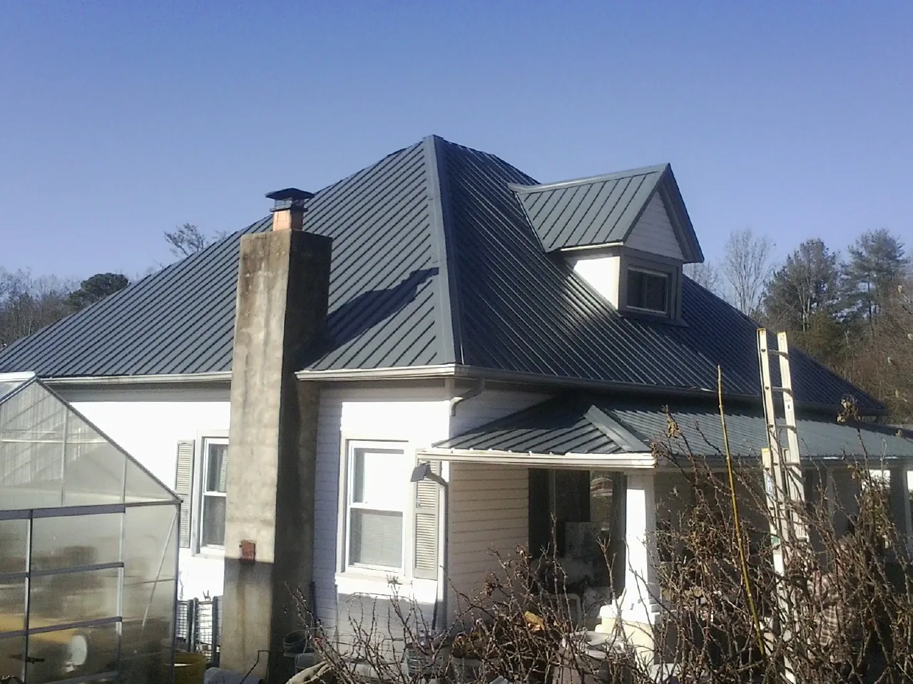 Dark blue standing seam metal roof on a white farmhouse with dormer — Slate & Tile Roof Repair by Roofing Brothers in Rosalie