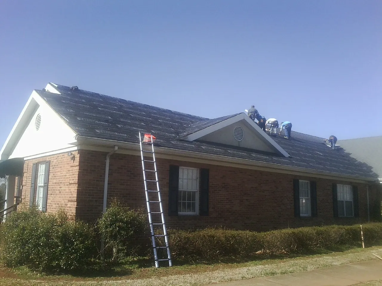 Crew tearing shingles off a brick ranch roof with a ladder set — Emergency Roof Repair work by our crew in Rosalie