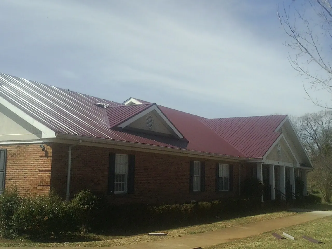 Red metal roof with gabled entries on a long brick building, from a Hail Damage Roof Repair job in Rosalie