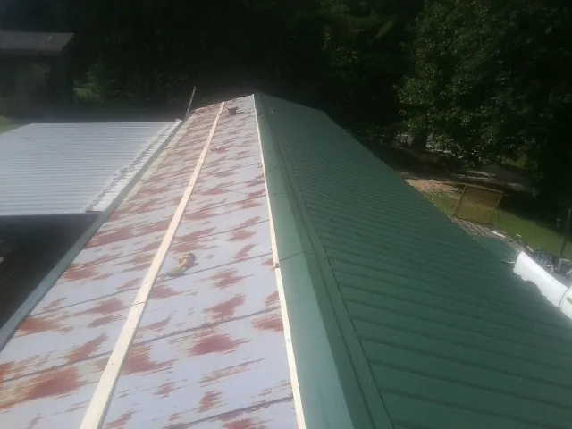 Old rusted panels beside newly installed green metal roofing — Wind Damage Roof Repair by Roofing Brothers in Rosalie