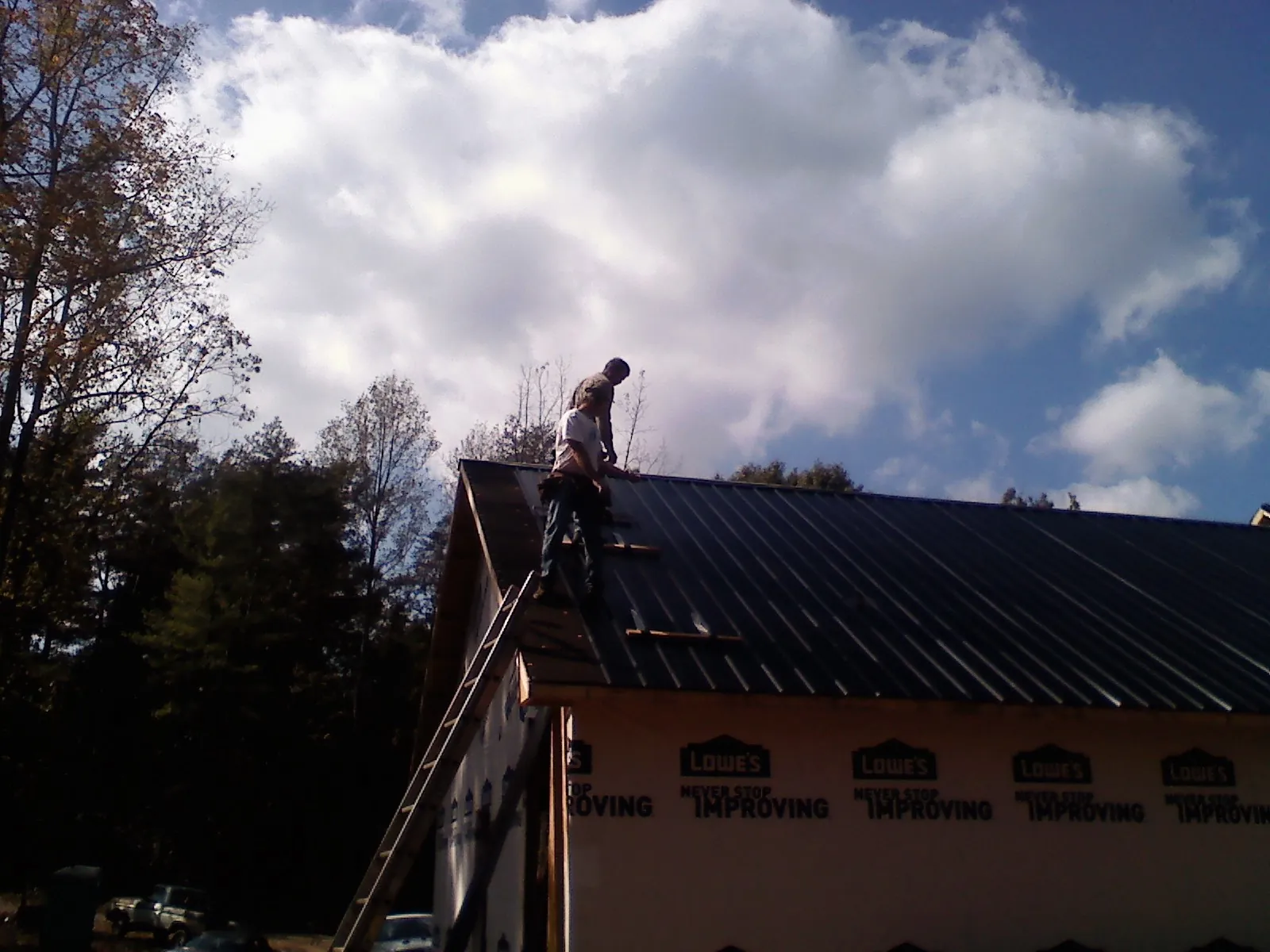 Roofer fastening dark metal panels high against a cloudy sky, from a Roof Inspection job in Rosalie