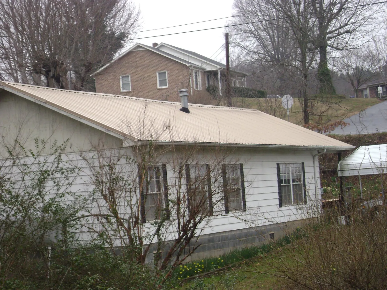 Tan metal roof on a white sided house set into a hillside — Commercial Roofing by Roofing Brothers in Rosalie